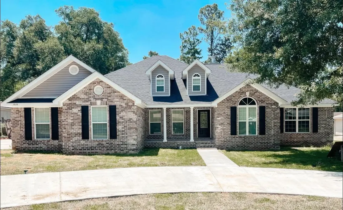 Brick home with two dormers, black shutters and a curved concrete walk