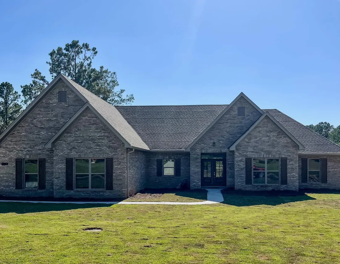 Gray brick ranch home with twin front gables and a new green lawn
