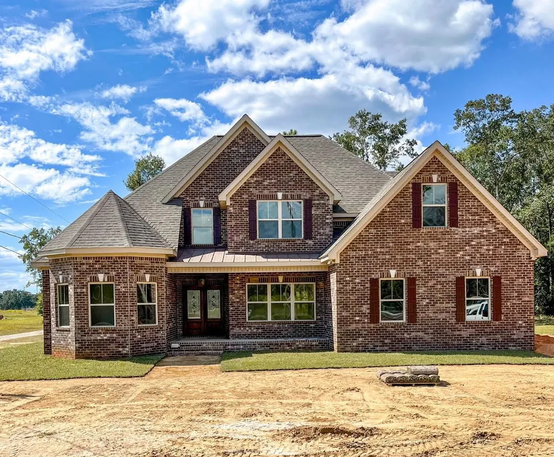 Two-story red brick home with gables, a turret-style bay and arched double front doors