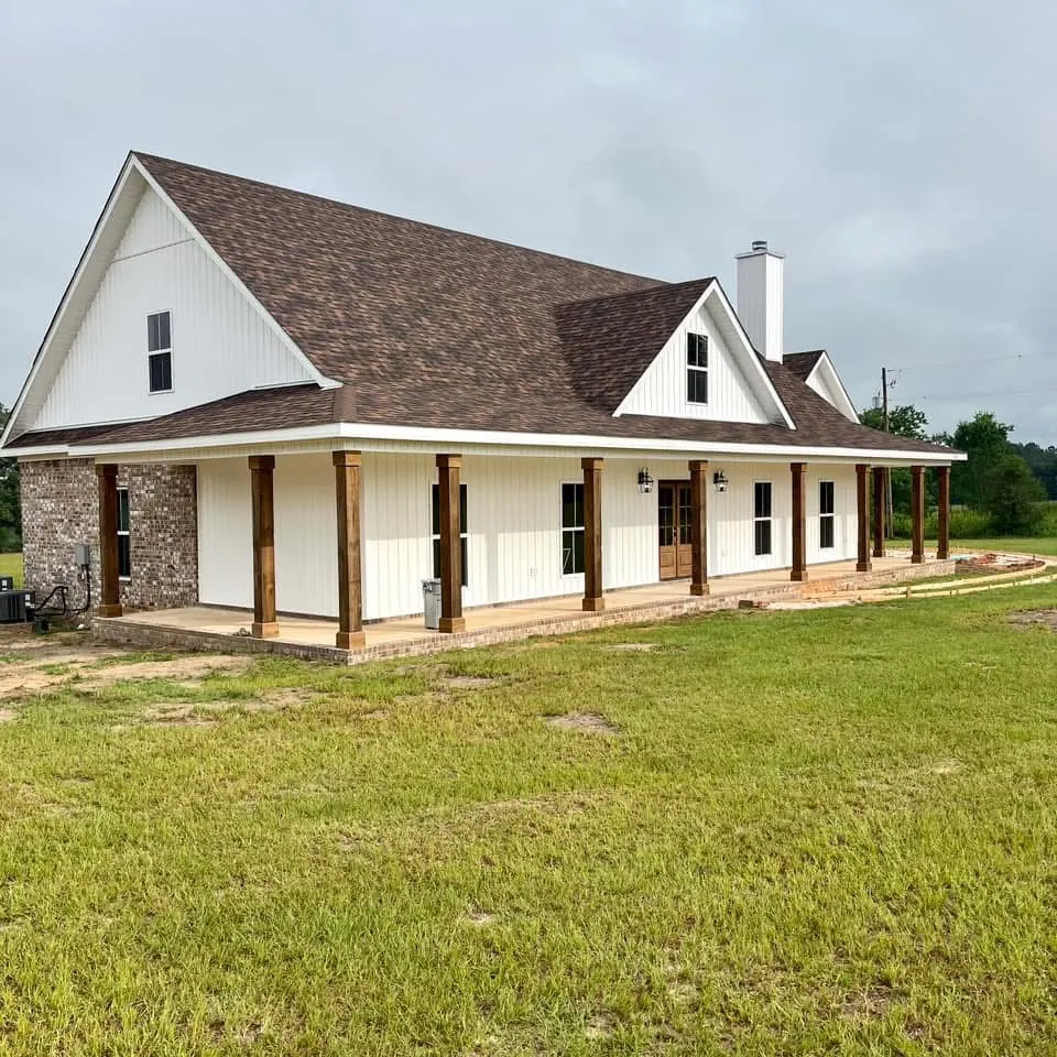 White farmhouse with steep gables, a stone chimney base and a porch on cedar posts