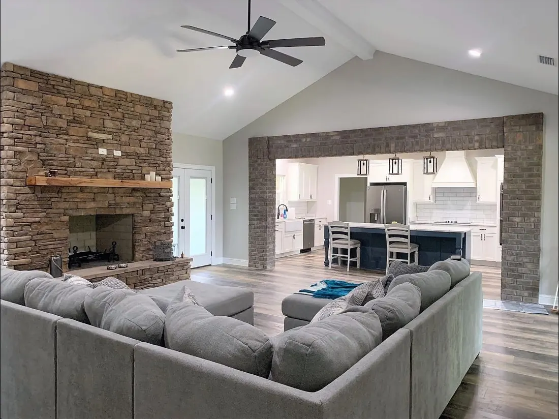 Open great room with a brick fireplace and a brick-framed opening into the kitchen