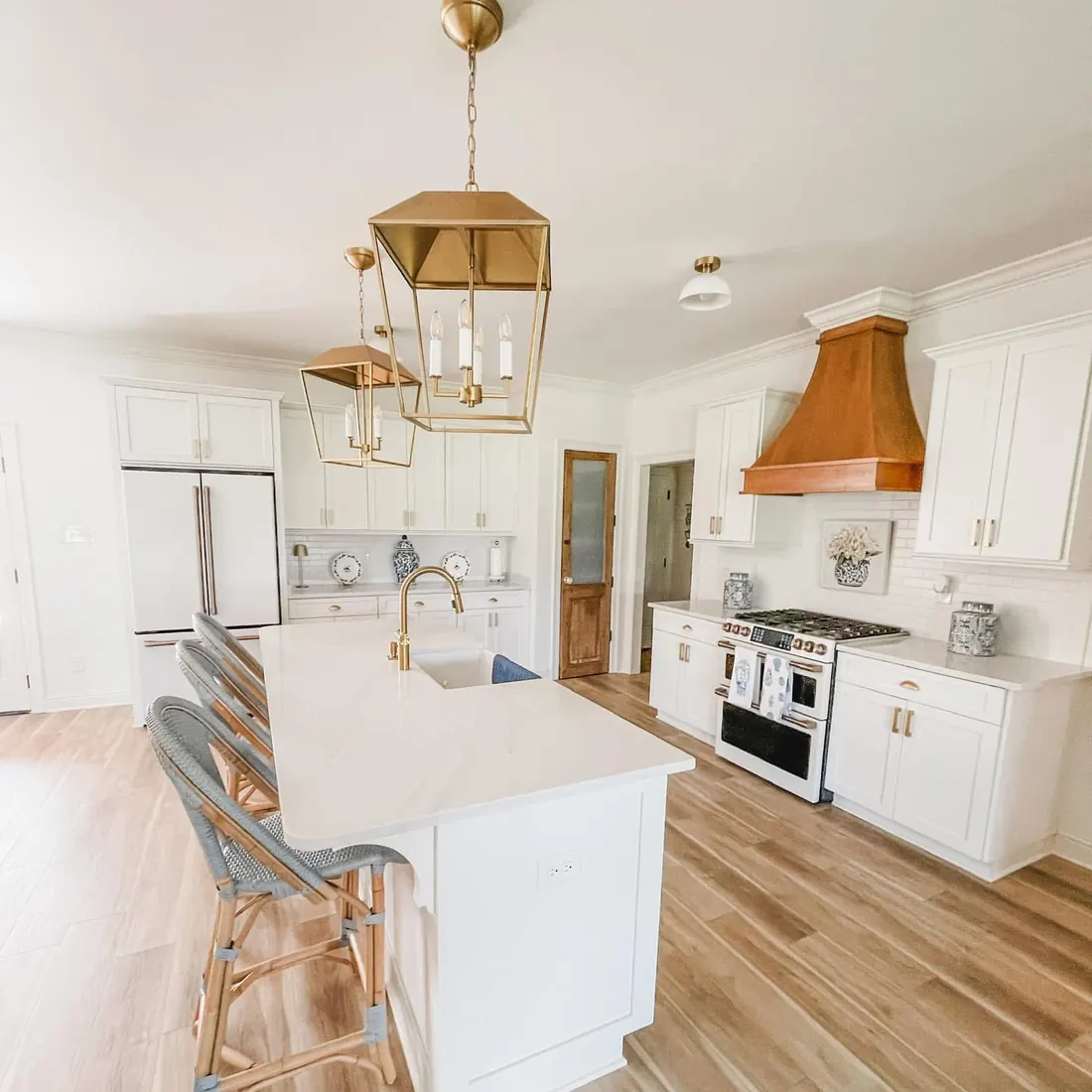 White kitchen with a large island, gold pendant lights and a copper range hood