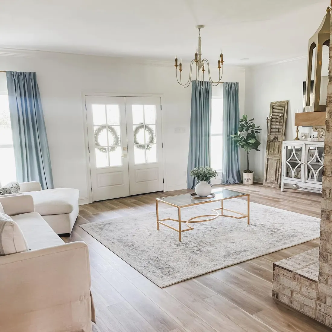 Bright living room with French doors, light wood floors and soft blue curtains