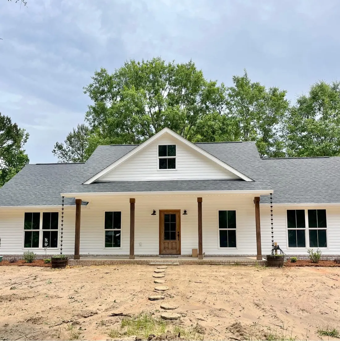 White farmhouse with a center gable, wood front door and cedar porch posts