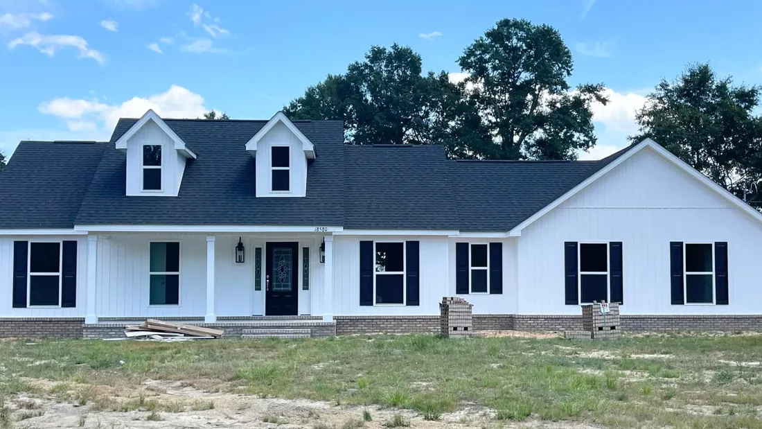 White board-and-batten home with two dormers, black shutters and a covered porch