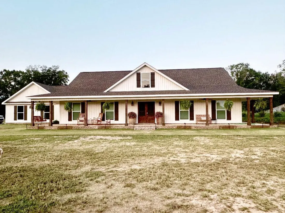 Long single-story home with a wraparound front porch, potted plants and a red front door