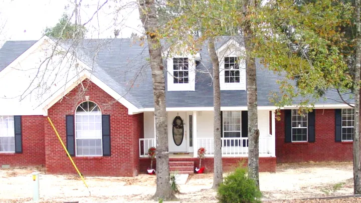The Pineridge plan: red brick home with a dormer and a front porch under pine trees